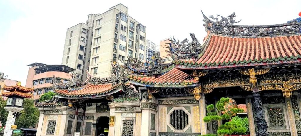 Il tetto del Longshan Temple, il padiglione dell'orologio e un pino in primo piano, contro i grattacieli della Taipei contemporanea